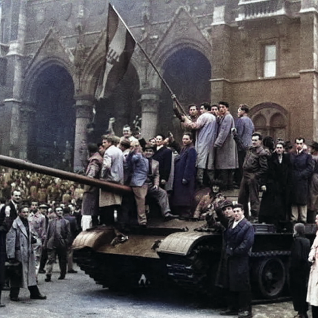 Hungarian revolutionaries standing atop a tank, waving their flag in a crowded square with a historic building in the backdrop.