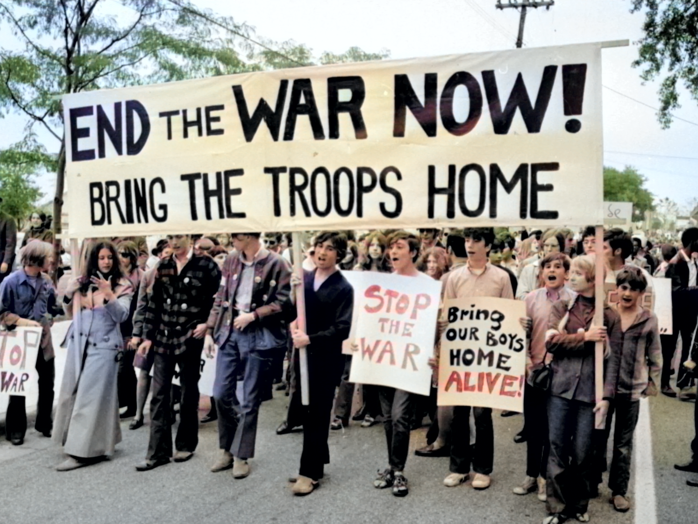 Protesters marching with a large sign that reads: 'end the war now. send the troops home' during the Moratorium to End the War in Vietnam.